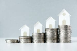Casas em miniatura sobre pilhas de moedas crescentes, representando valorização imobiliária ou investimento no setor.